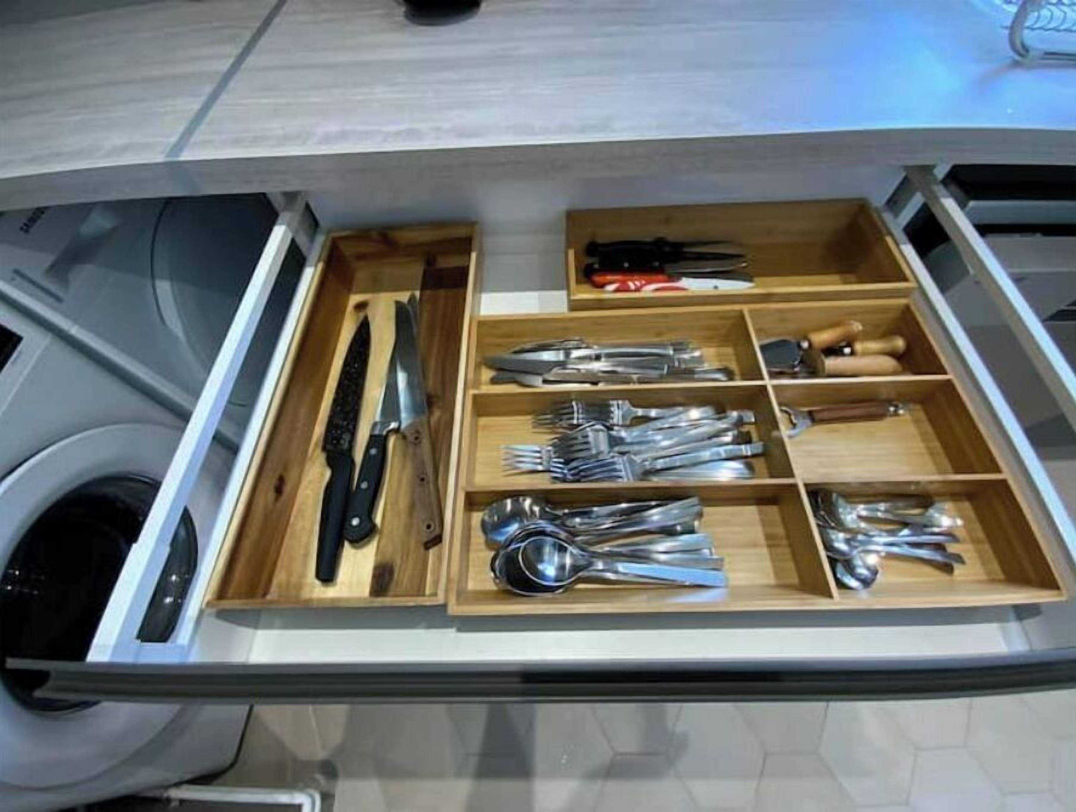 A drawer with various kitchen utensils including knives, forks, spoons, and a grater.