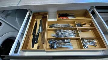 A drawer with various kitchen utensils including knives, forks, spoons, and a grater.