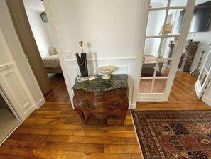 Un plancher en bois, une table d’appoint au plateau en marbre ornée d’un vase et d’un livre, et un tapis à motifs.