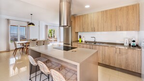 A modern kitchen with a central island, wooden cabinets, and a stainless steel range hood. - Villa Las Arenas with private heated pool (Salobreña)