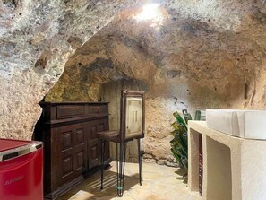 A stone-walled room with a wooden cabinet, a small table, and a red trash bin.