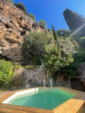 A swimming pool with a wooden deck, surrounded by greenery and rocky cliffs.
