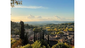 Une vue panoramique d’une ville à l’architecture traditionnelle, avec des maisons à étages et de grands cyprès.
