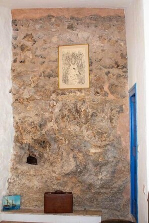 A stone wall with a framed picture and a brown suitcase on a ledge.