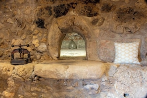 Une pièce aux murs de pierre, avec un banc de pierre, un four en pierre et un coussin décoratif.