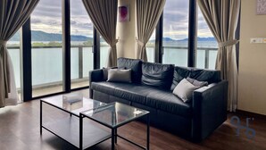 A modern living room with a leather sofa, a glass coffee table, and large windows with curtains. - Homesuite’ Home @ Riverson SOHO (Kota Kinabalu)