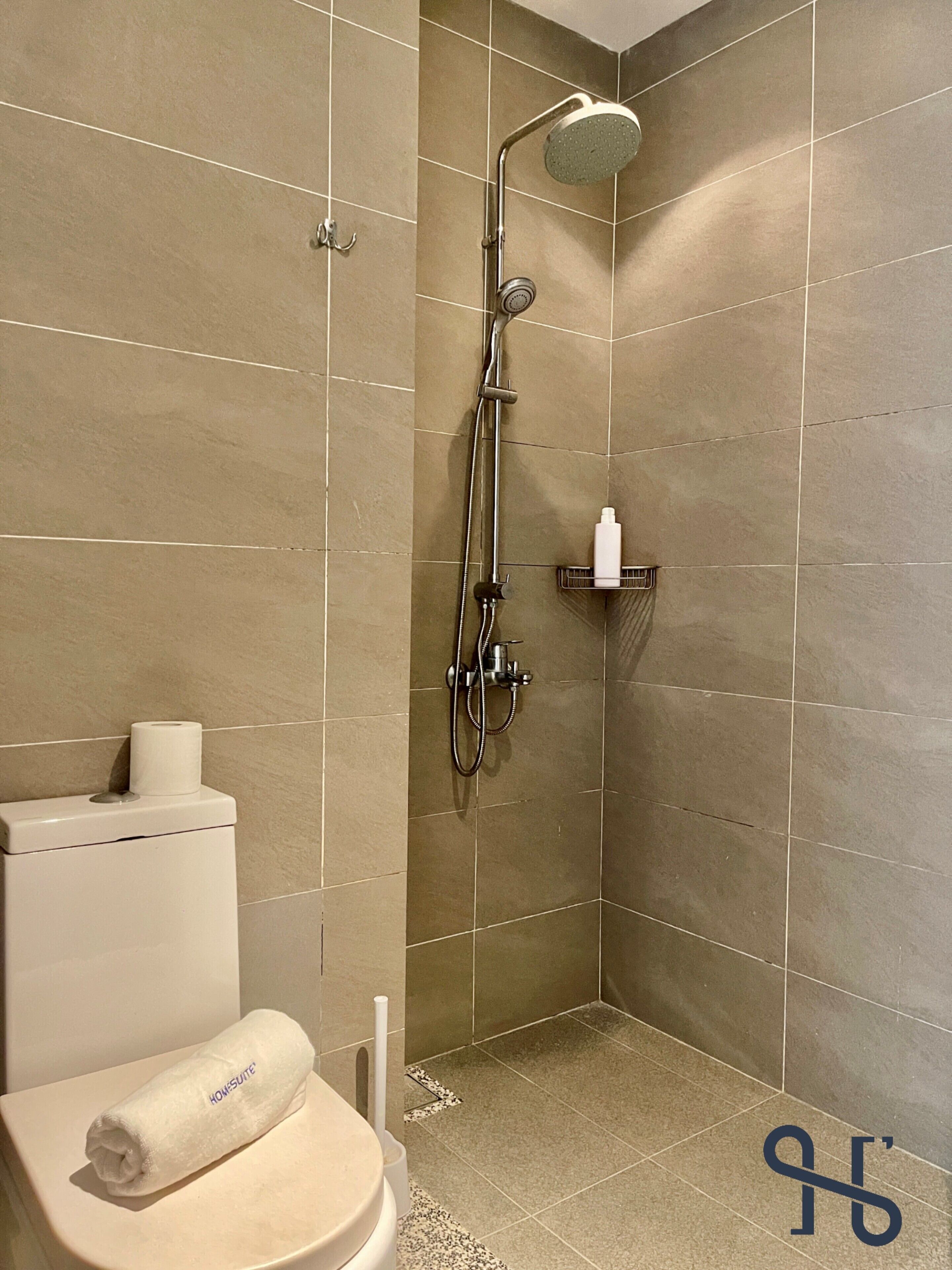A bathroom with a shower, toilet, and a towel on the seat.