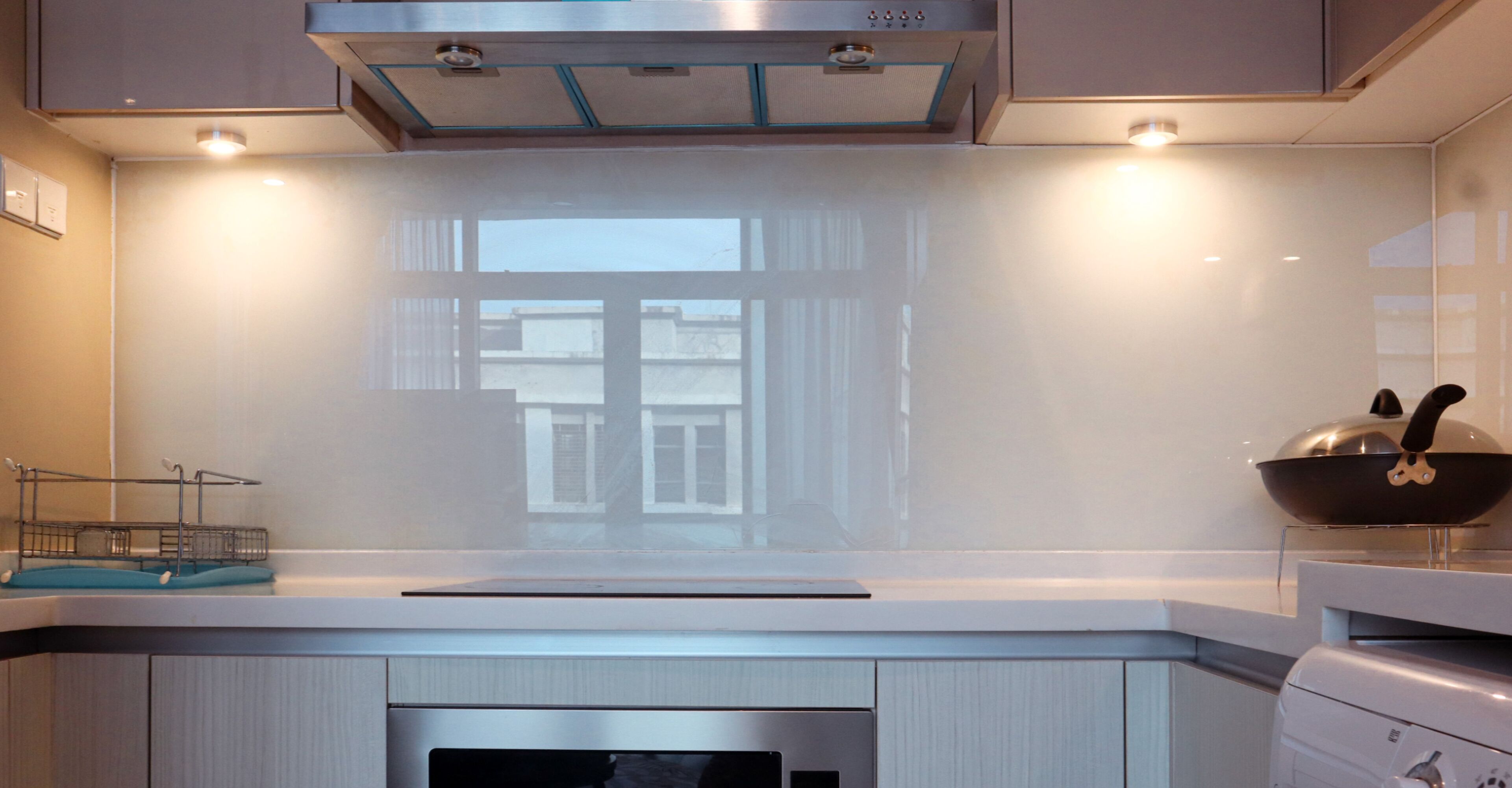 Una cocina moderna con una campana extractora de acero inoxidable, un ventanal con vistas a edificios y un wok sobre la estufa.
