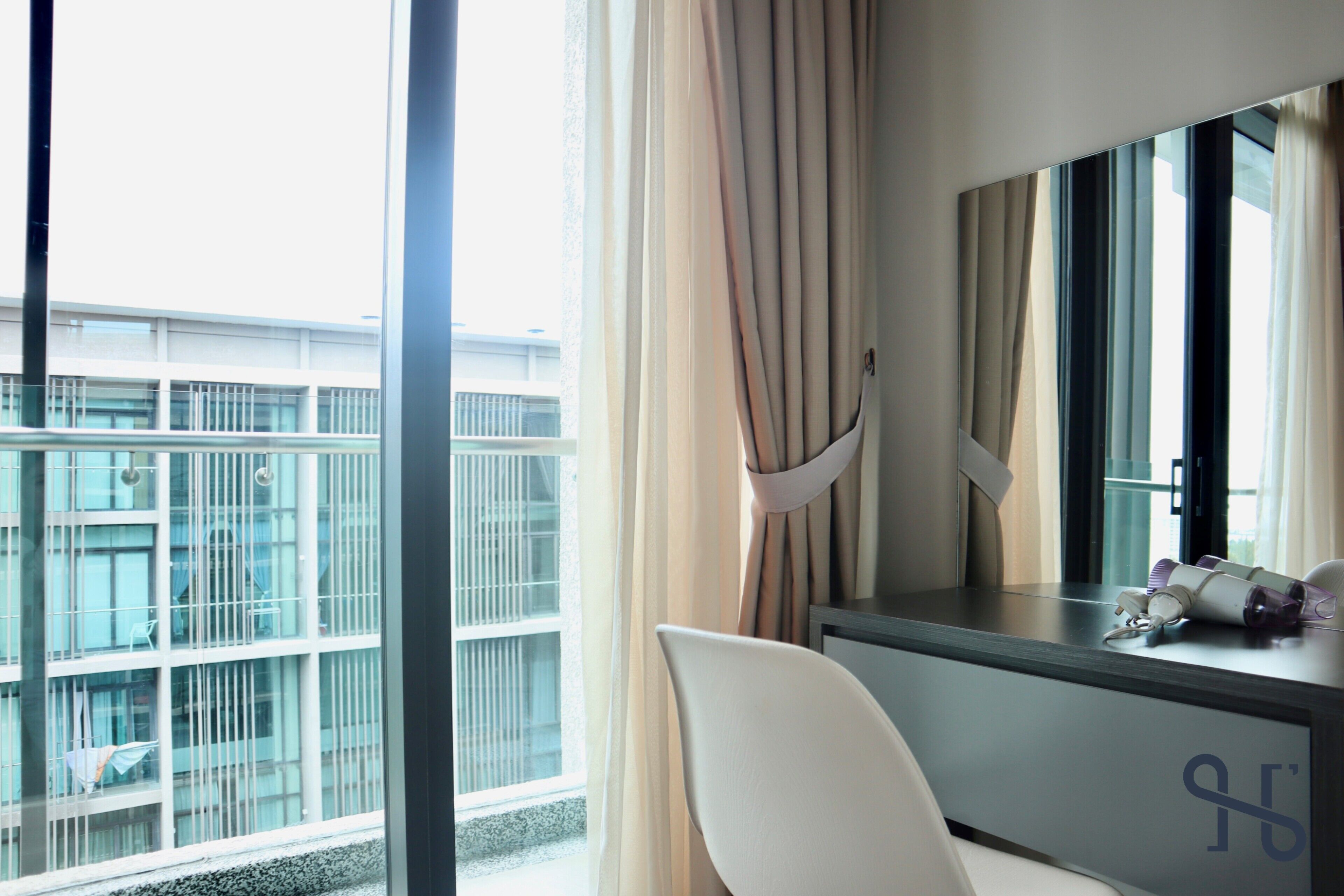 Une chambre d’hôtel avec une grande fenêtre, un bureau doté d’un miroir et une chaise.