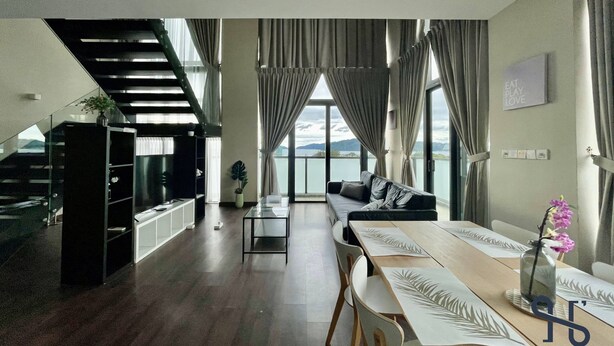 A modern living room with a staircase, a dining area, and large windows offering a view of the outdoors. - Homesuite’ Home @ Riverson SOHO (Kota Kinabalu)