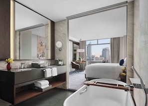 A modern hotel bathroom with a bathtub, a vanity with a mirror, and a city view through the window. - Chatrium Grand Bangkok (Bangkok)