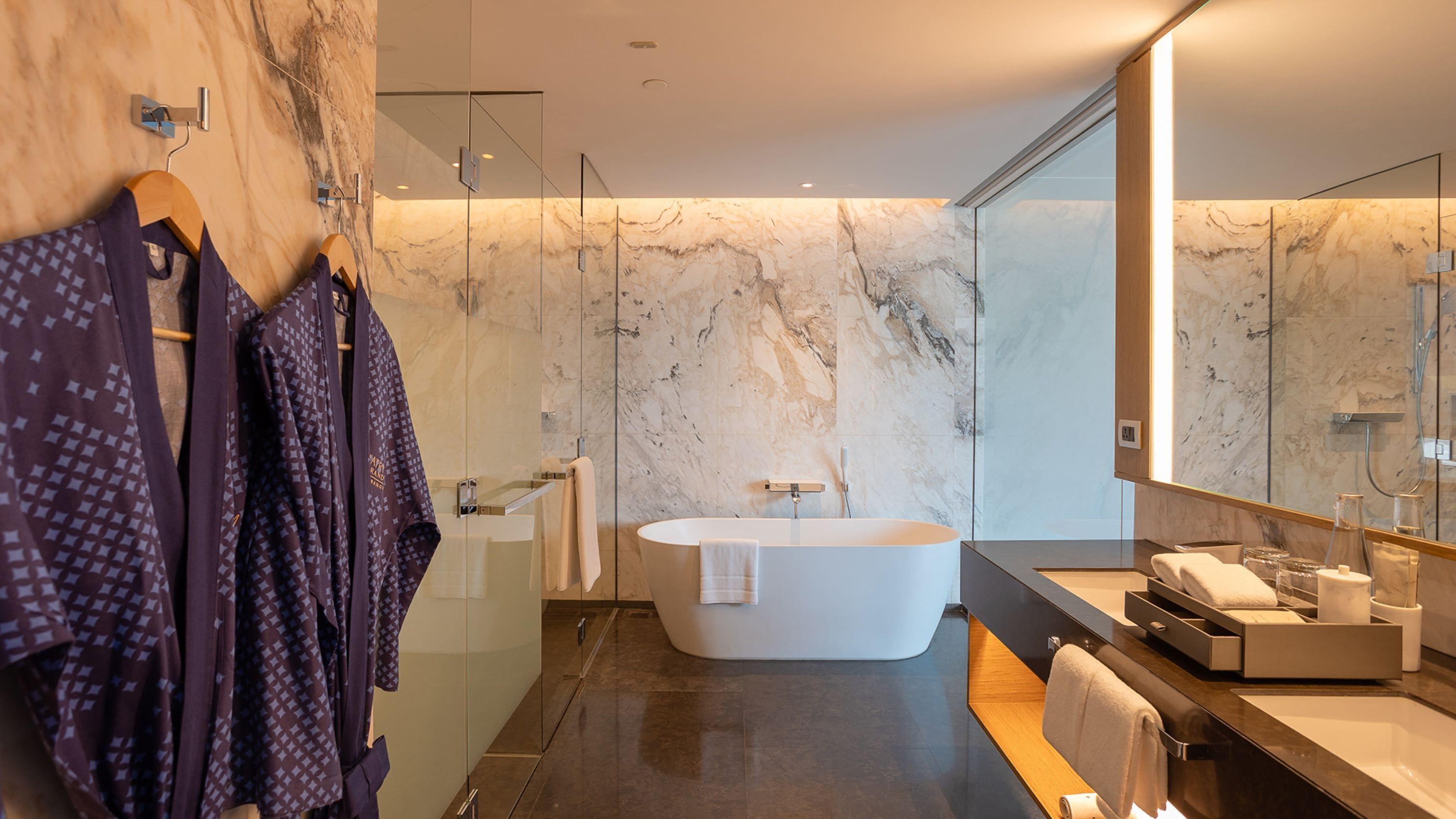 A modern bathroom with a freestanding bathtub, marble walls, and a large mirror.