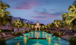 A swimming pool with lounge chairs and palm trees, surrounded by buildings. - Chatrium Grand Bangkok (Bangkok)
