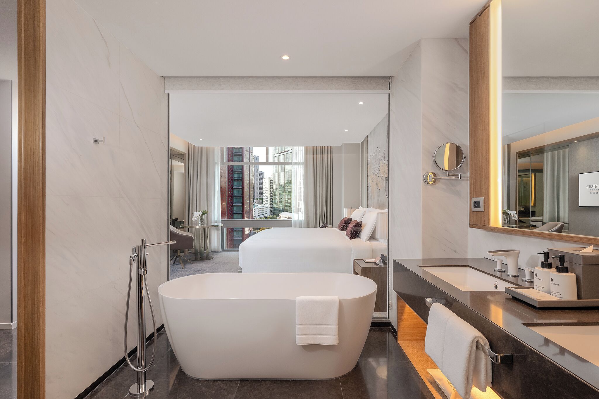 Un baño moderno con una bañera grande, un tocador con espejo y una cama al fondo.