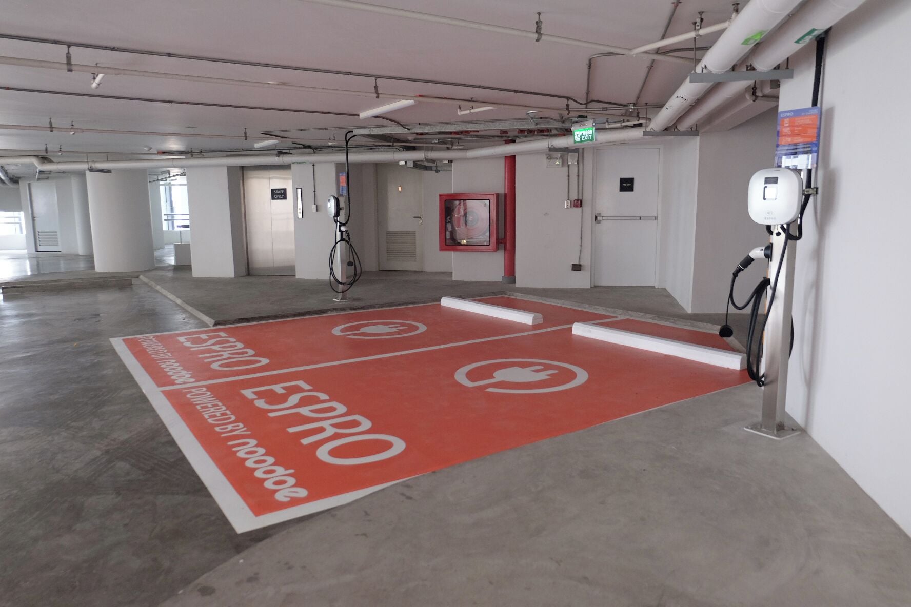 A parking area with electric vehicle charging stations, a red floor marking, and a sign indicating an exit.