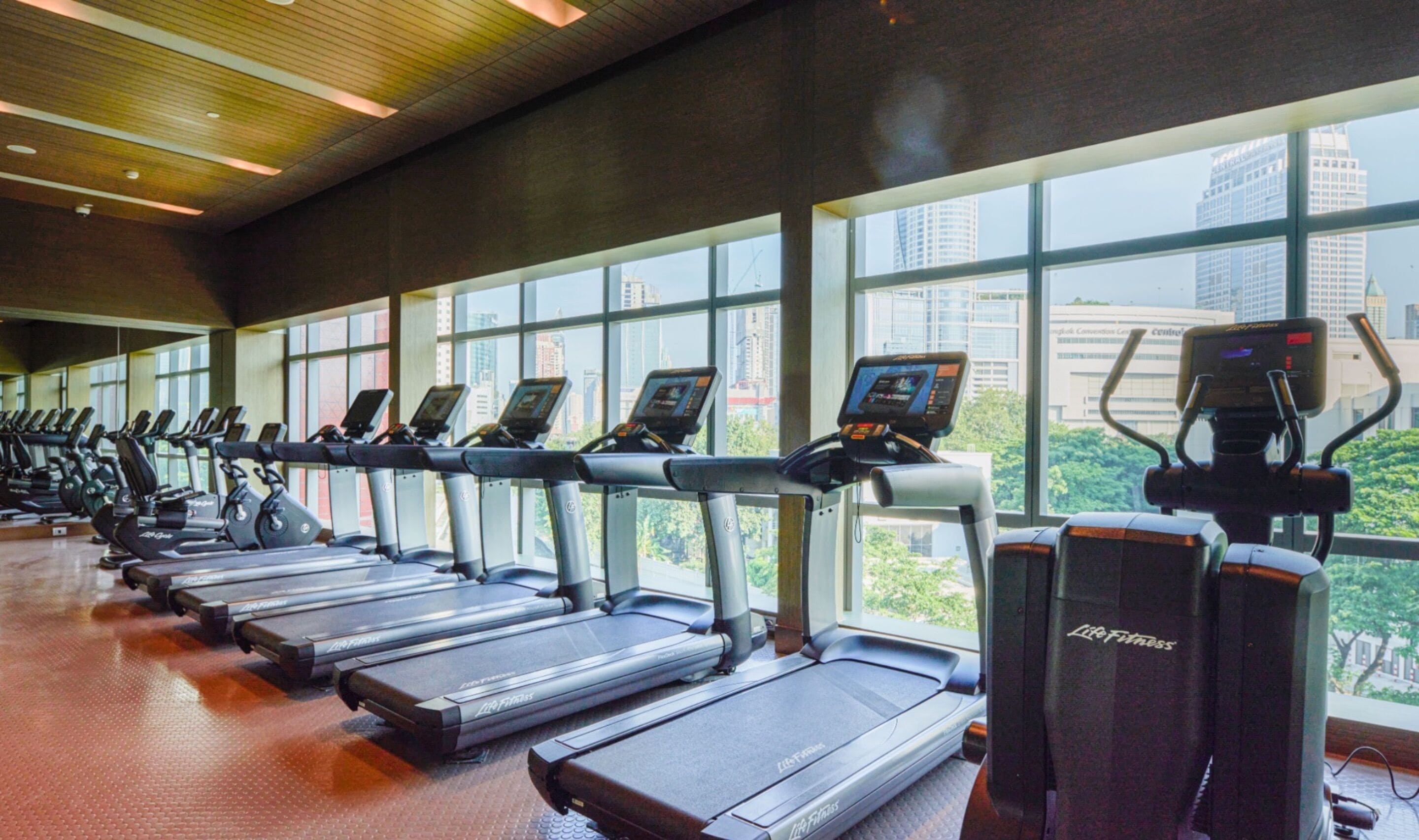A gym with treadmills and elliptical machines, large windows, and a city view.