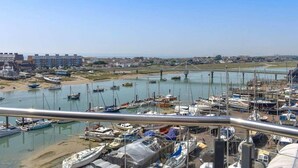 A marina with numerous boats docked, a bridge in the background, and buildings along the shore.