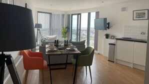 A modern kitchen with white cabinets, a dining area with a table and chairs, and a large window offering a city view.