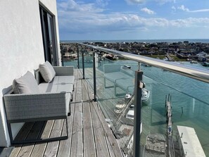 A balcony with a glass railing overlooking a marina with boats and a distant cityscape.