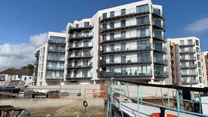 A multi-story residential building with balconies, a concrete foundation, and construction materials visible in the foreground.