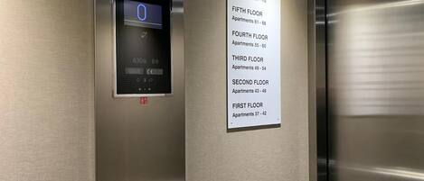 Intérieur d’un ascenseur doté d’un écran numérique, d’une signalétique indiquant les numéros d’urgence et d’une signalétique indiquant les étages.