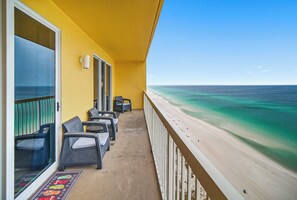 Un balcon agrémenté de meubles en osier, une vue sur la plage et un ciel dégagé.