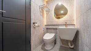 A modern bathroom with a toilet, sink, and towel rack against a wooden panel wall. - Yeosu Liposo Poolvilla (Yeosu)