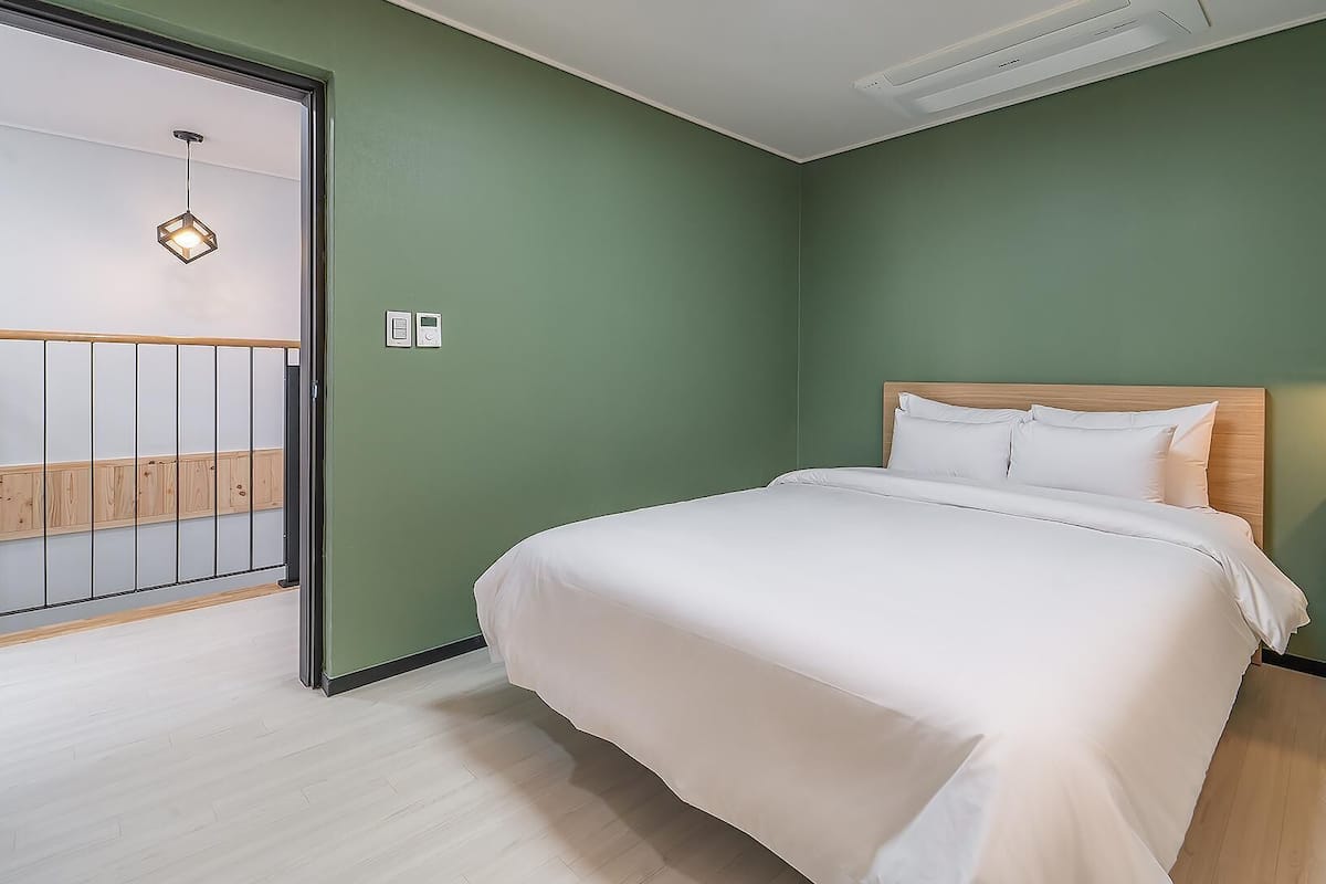 Un dormitorio con cama, mesita de noche, pared verde, cabecero de madera y puerta al balcón.