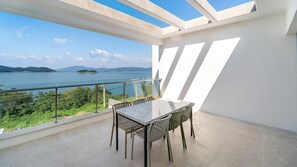 A balcony with a table and chairs, overlooking a body of water and greenery. - Yeosu Liposo Poolvilla (Yeosu)