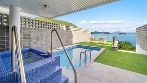 A rooftop pool with blue-tiled steps, a view of the sea, and a grassy area with lounge chairs. - Yeosu Liposo Poolvilla (Yeosu)
