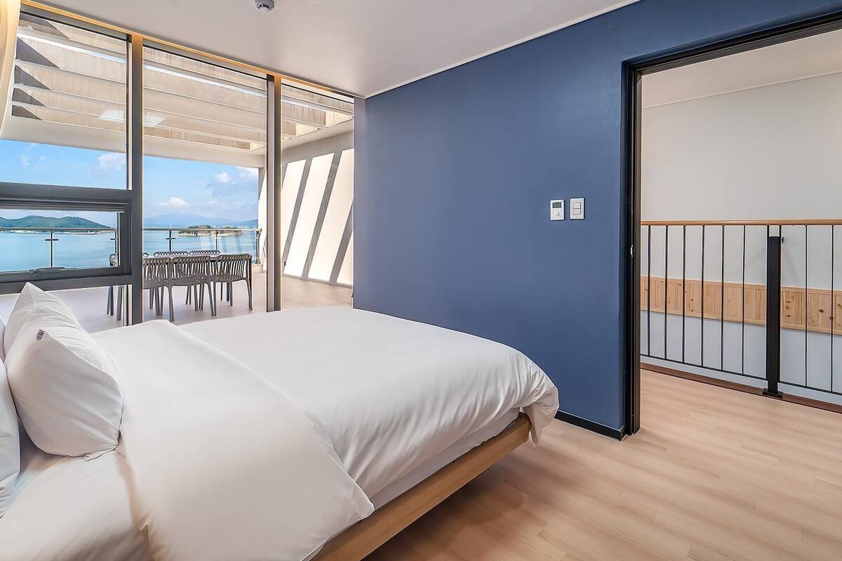Un dormitorio con cama, vistas al mar, un balcón con sillas y una puerta corrediza.