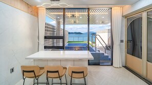 A modern room with a white table and three chairs, a sliding glass door leading to a balcony with a pool and a view of the sea. - Yeosu Liposo Poolvilla (Yeosu)