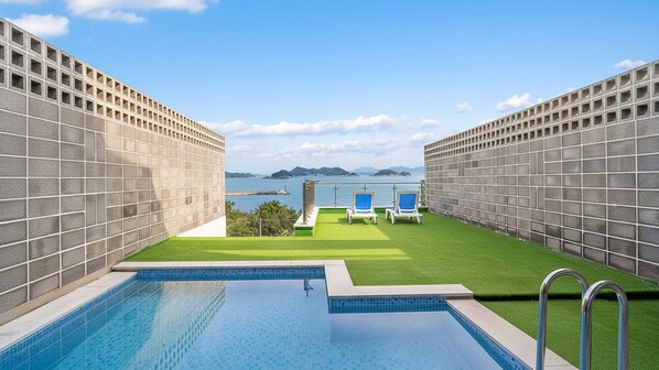 A swimming pool with two lounge chairs and a view of the sea. - Yeosu Liposo Poolvilla (Yeosu)
