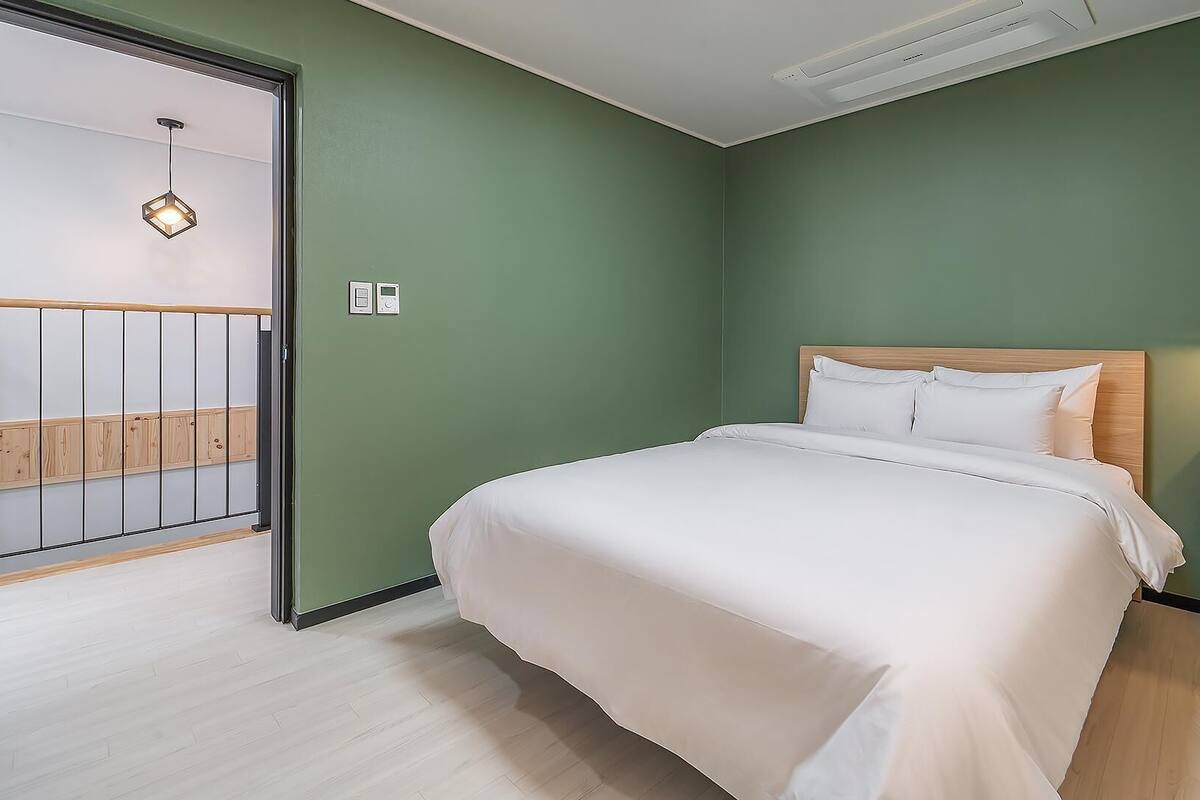 Un dormitorio con cama, mesita de noche, pared verde, cabecero de madera y puerta al balcón.