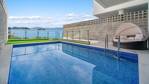 Ein Swimmingpool mit Meerblick, eine überdachte Sitzgelegenheit und eine geflieste Wand.