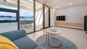 Ein modernes Wohnzimmer mit einem großen Schiebeglastür, die auf einen Balkon mit Blick auf das Meer und die Berge führt.