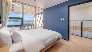 Ein Schlafzimmer mit einem großen Bett, Meerblick und einem Balkon mit Sitzgelegenheiten.