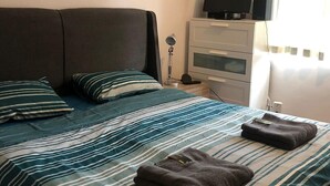 Quarto de hotel com cama, televisão, escrivaninha e janela com cortinas.