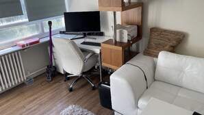 Um espaço de escritório moderno com uma mesa branca, computador e cadeira, um sofá branco e uma estante de madeira.
