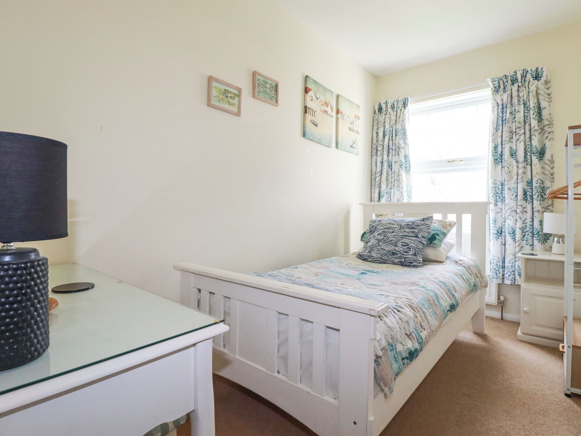 A bedroom with a single bed, a bedside table with a lamp, and a window with curtains.