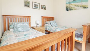 A bedroom with two wooden beds, a nightstand, and a wooden bench. - 2 Old Talbot Cottages (Lostwithiel)