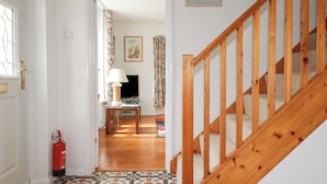 A staircase with wooden railings leading to a living room with a television, a table, and patterned curtains. - 2 Old Talbot Cottages (Lostwithiel)