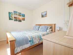 A bedroom with a wooden bed, a bedside table, and a wall with three paintings. - 2 Old Talbot Cottages (Lostwithiel)