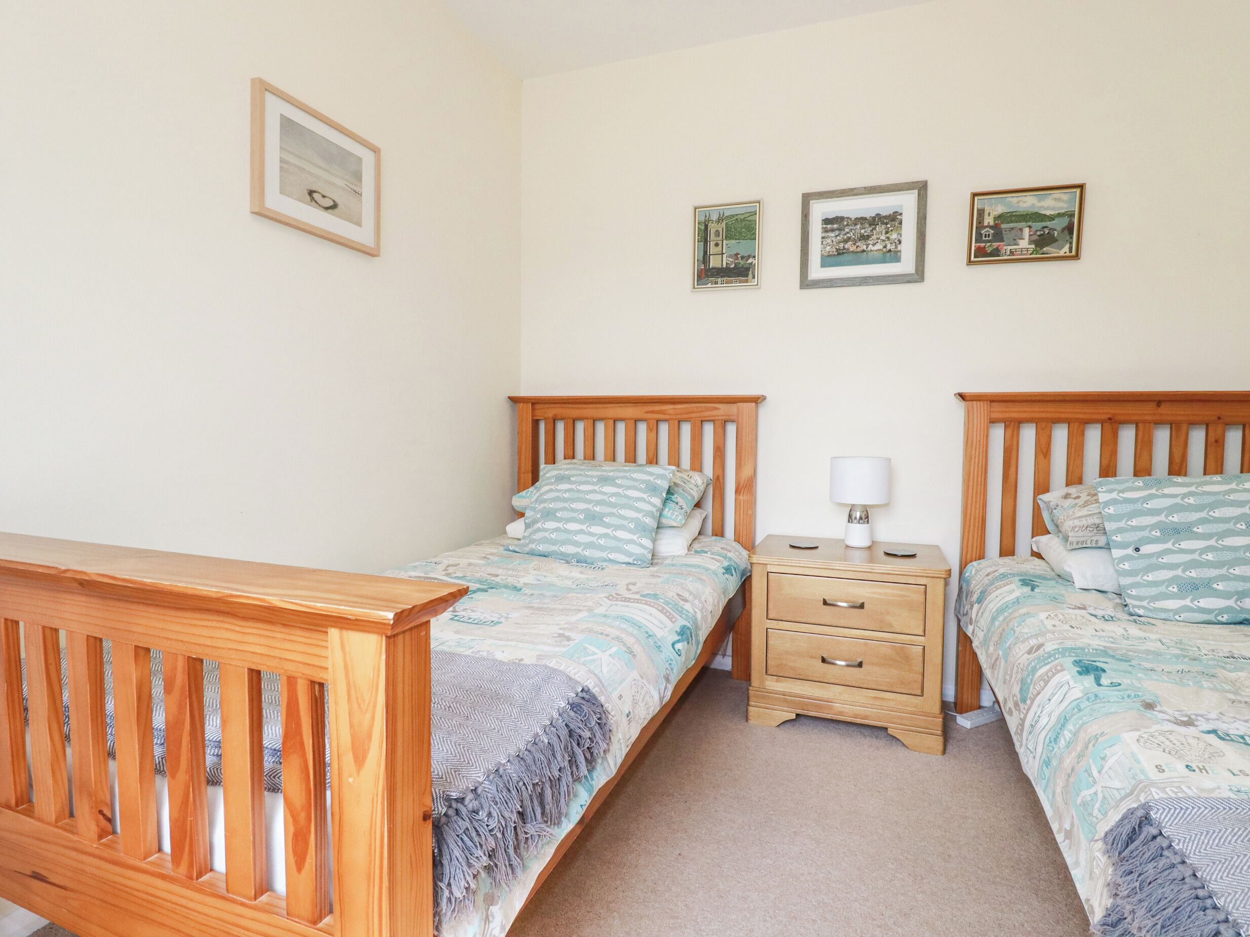 A bedroom with two wooden beds, a nightstand with a lamp, and three framed pictures on the wall.