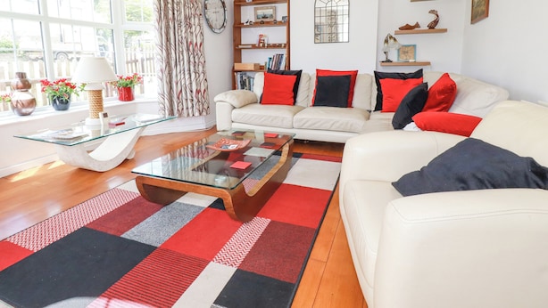 A living room with a white sofa, red and black cushions, a glass coffee table, and a patterned rug. - 2 Old Talbot Cottages (Lostwithiel)