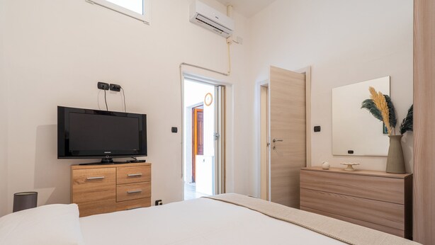A bedroom with a bed, a TV on a wooden dresser, a mirror on a dresser, and a door leading to another room. - 2978 La Dea Venere by Barbarhouse (Nardò)