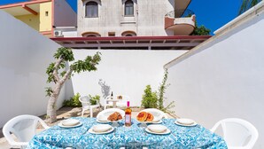 An outdoor dining area with a table set for two, surrounded by white chairs, under a clear blue sky. - 2978 La Dea Venere by Barbarhouse (Nardò)