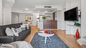 Una sala de estar moderna con un sofá negro, una mesa de centro redonda y un televisor de pantalla plana montado en la pared.