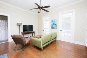 Ein Wohnzimmer mit einem grünen Sofa, einem braunen Sessel, einem Holztisch, einem Fernseher auf einem Schrank und einem Deckenventilator.