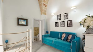 A room with a teal sofa, framed pictures on the wall, and a staircase with a rope barrier. - 2666 La Maisonnette - Appartamento 1 (Nardò)